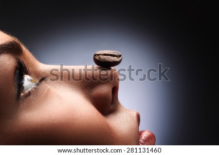 A black roasted coffee bean on the nose of a beautiful girl smelling coffee and relaxing.