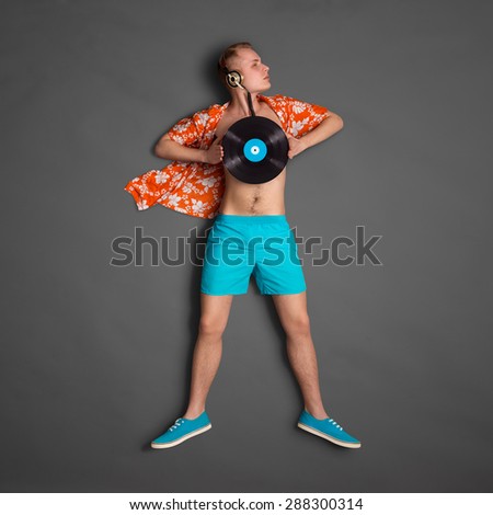 Photo of a male fashionable handsome hipster as a superhero, wearing vintage music headphones and holding an LP microgroove vinyl record on dark background.