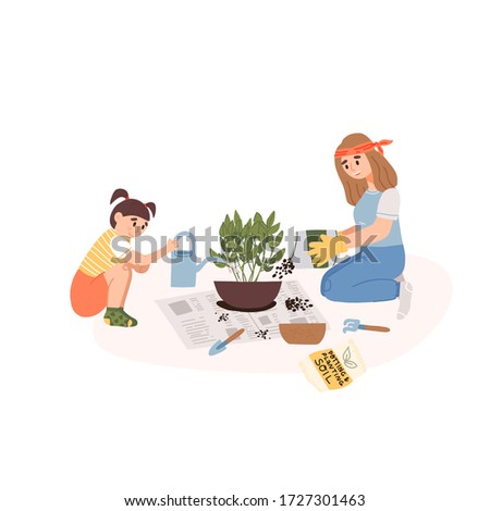 Cute little girl in t-shirt help her mother in garden gloves to transplant a house plant on a newspaper in a larger pot at home in the living room and pours water from a pot.