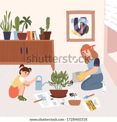 Cute little girl in t-shirt help her mother in garden gloves to transplant a house plant on a newspaper in a larger pot at home in the living room and pours water from a pot.