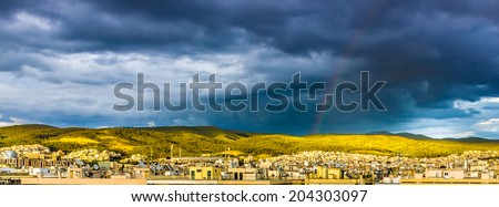 Beautiful panorama view of city roofs under the stormy sky with rainbow and green hills on the background.Thessaloniki, Greece