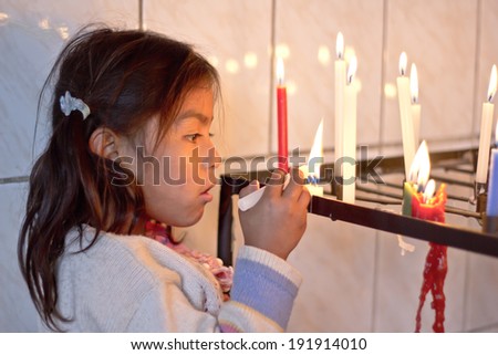 SUCRE, BOLIVIA - JANUARY 18, 2012: A girl lights a candle inside a little improvised chapel. January 18, 2012. in Sucre, Bolivia. the vast majority of Bolivian people are Roman Catholics.