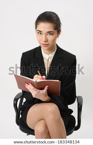 business woman sitting in an office chair and writing in pencil in a notebook