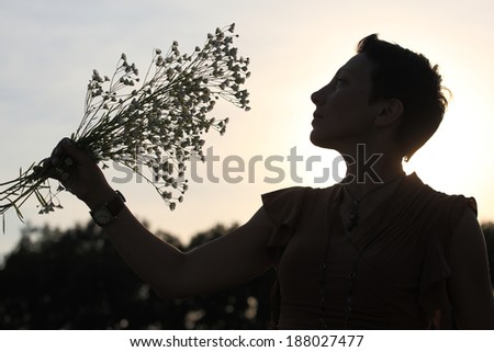 A silhouette of a beautiful girl holding flowers in the meadow at sunset