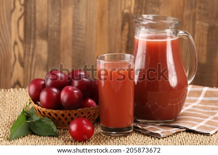 plum juice in a glass and pitcher, plums in a wicker basket on a mat and boards