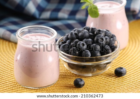 yogurt with blueberries in a glass jar and blueberries in a glass bowl on a background of yellow wicker mat