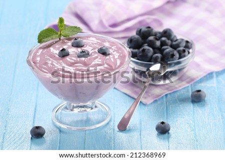 yogurt with blueberries in a glass bowl and blueberries in a glass bowl on a wooden background painted boards