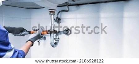 Technician plumber using a wrench to repair a water pipe under the sink. Concept of maintenance, fix water plumbing leaks, replace the kitchen sink drain, cleaning clogged pipes is dirty or rusty. Stockfoto © 