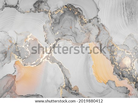 Luxury abstract fluid art painting in alcohol ink technique. Transparent layers of gray, yellow and gold paints create marbled texture of stripes, swirls and veins with glowing gold and glitter.