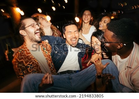 A multicultural group of friends are lifting their male tipsy friend at the rooftop night outdoor party. Foto d'archivio © 