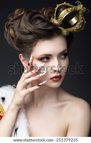 Beautiful girl in the image of the Queen in the mantle with a crown on the head and long nails. Beauty face. Picture taken in the studio on a gray background.