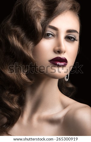 Beautiful woman with evening make-up, burgundy lips and curls. Beauty face. Picture taken in the studio on a black background.
