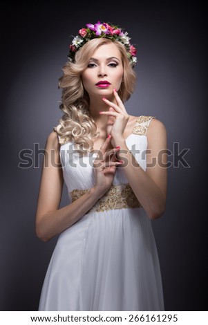 Beautiful blond girl in the image of a bride with flowers in her hair. Picture taken in the studio on a grey background. Beauty face