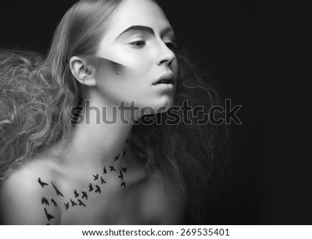 Beautiful girl with a pattern on the body in the form of birds, creative makeup and hairstyle lush. Beauty face. Black and white photo. Picture taken in the studio on a gray background.