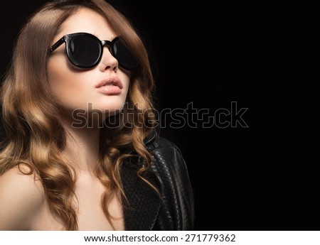 Beautiful girl in dark sunglasses, with curls and evening makeup. Beauty face. Picture taken in the studio on a black background.