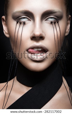 Beautiful girl with creative make-up in Gothic style and the threads of eyes. Art beauty face. Picture taken in the studio on a black background.