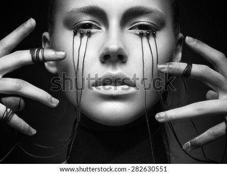 Beautiful girl with creative make-up in Gothic style and the threads of eyes. Art beauty face. Picture taken in the studio on a black background. Black and white photo