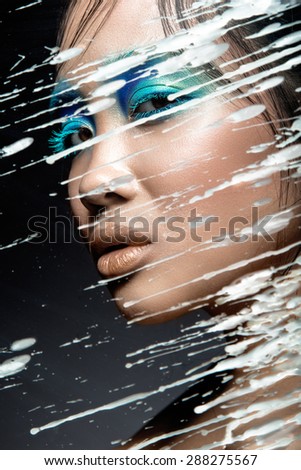 Beautiful Asian girl with bright blue make-up behind glass with drops of wax. Beauty face. Picture taken in the studio on a black background.