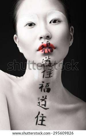 Beautiful Asian girl with white skin, red lips and hieroglyphics on her face. Art Beauty image.