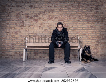Young man sitting on a bench with your best four-legged friend peering straight into the camera. With bricks texture and marble floors.