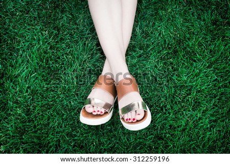 A pair of human legs (female) with shoes lying crosswise in a soft, deep green grass.