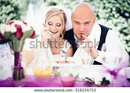 Bride and groom with soup at wedding feast. Newlyweds have a funny moment during the feeding of each other with happy expressions in their faces. (Focused on eyes of newlyweds, shallow depth of field)