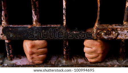 Mans hands grabbing onto old rusted bars with face hidden in darkness