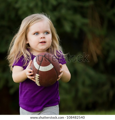 Young girl playing in the backyard running with her football