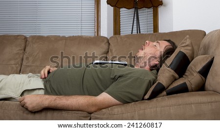 Fat obese man fell asleep on the couch with a remote on his chest