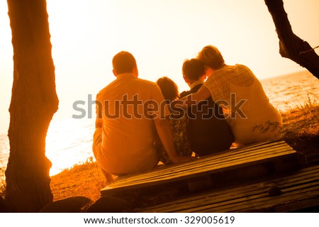 Loving parents holding their children and watching the sunset together. Family relaxing in nature and enjoying a beautiful view of the sun setting over the sea. Concept of love and togetherness