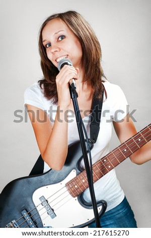 Girl with mic and bass guitar isolated on gray background