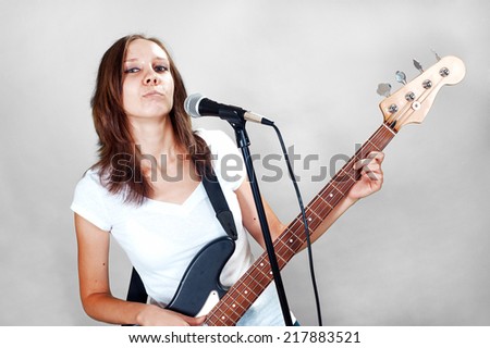 Girl with microphone and bass guitar isolated on gray background