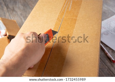 A view of a hand holding a box cutter tool prepping to open a cardboard box shipment package. ストックフォト © 