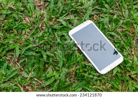 White smart phone with blank screen on green grass background