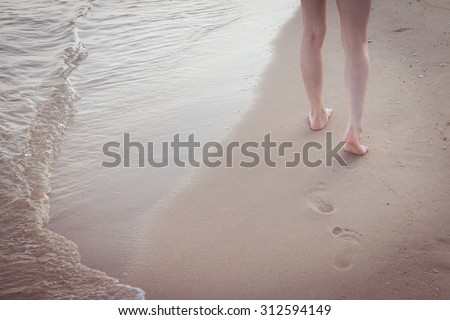 Beach travel alone - woman walking alone on sand beach leaving footprints in the sand Closeup detail of female feet and golden sand background
