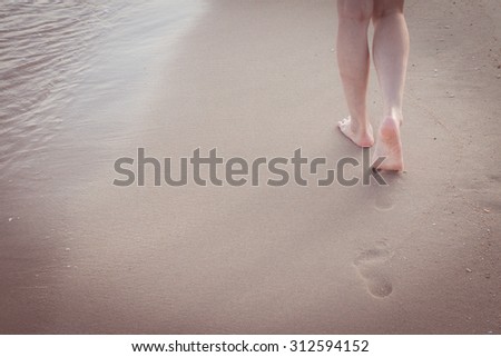 Beach travel alone - woman walking alone on sand beach leaving footprints in the sand Closeup detail of female feet and golden sand background