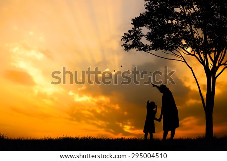 A silhouette of a happy family, mother,girl and infant (women pregnancy) with tree on blurred sunset sky on mountain (copy space or text on left area)