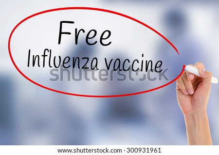 Hand writing Free Influenza Vaccine with marker on transparent board over blurred medicine injection.