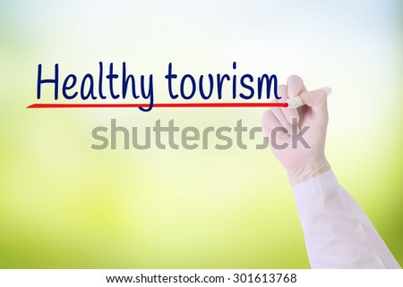 Doctor hand with Glove writing Health tourism over green blurred background