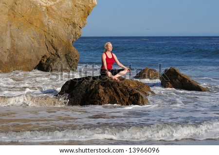 Young oman performs yoga meditation on a rock in the surf, facing the sun.