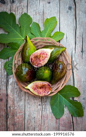 Fresh figs with green leaves in the wattled plate on a rustic wooden board