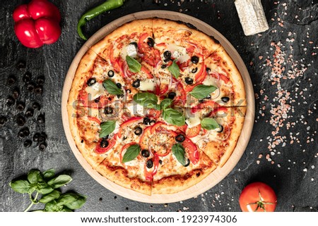 Hot tasty traditional italian pizza with salami, meat, cheese, tomatoes greens on a dark background