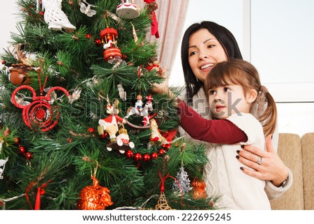 A young girl helps her mother to decorate the family Christmas tree