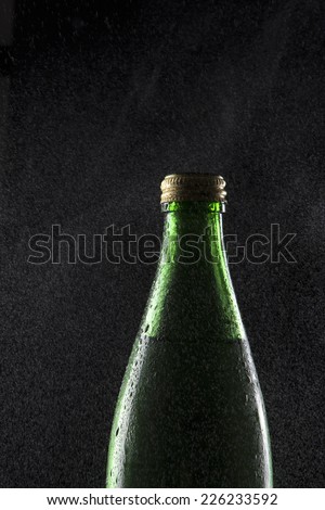 A green glass container with carbonated soft drink and water vapor on isolated black.