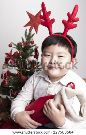 A asian(korea, japan, chinese, china) boy hold(hug) christmas socks for presents and wearing christmas hat with big smile isolated white at the studio and christmas tree.