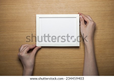 A female(woman) hands hold a white wood photo(picture) empty(blank) frame on the desk at the studio.