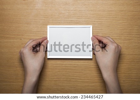 A female(woman) hands hold a steel photo(picture) empty(blank) frame on the desk(table)  top view at the studio.
