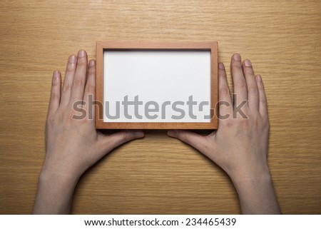A female(woman) hands hold a wood photo(picture) empty(blank) frame on the desk(table), top view at the studio.