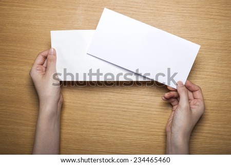 A female(woman) hands hold a empty(blank) white letter and envelope on the desk(table), top view at the studio.