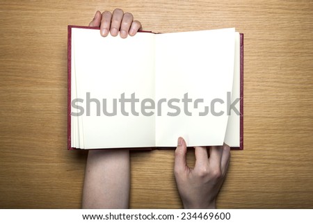 A female(woman) hands hold a blank(empty) book(note, diary) on the wood desk(table), top view at the studio.